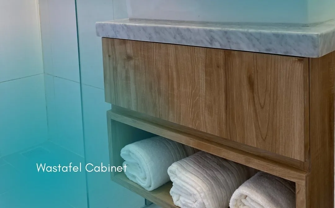 Bathroom vanity with a marble top and a wood cabinet holding folded towels